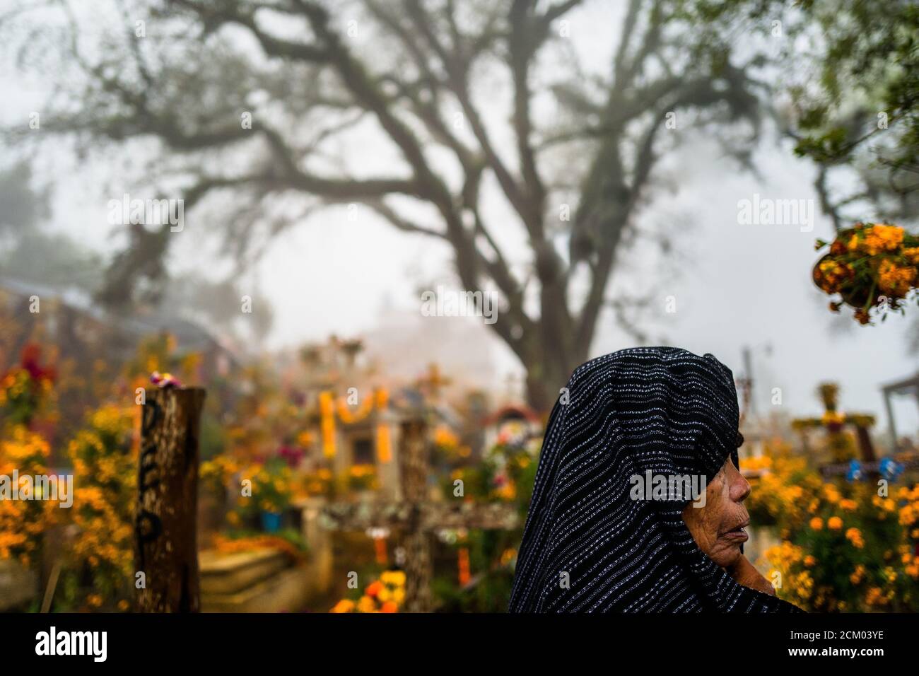 Una donna indigena messicana cammina tra le tombe decorate con fiori in un cimitero durante le celebrazioni del giorno dei morti ad Ayutla, Messico. Foto Stock