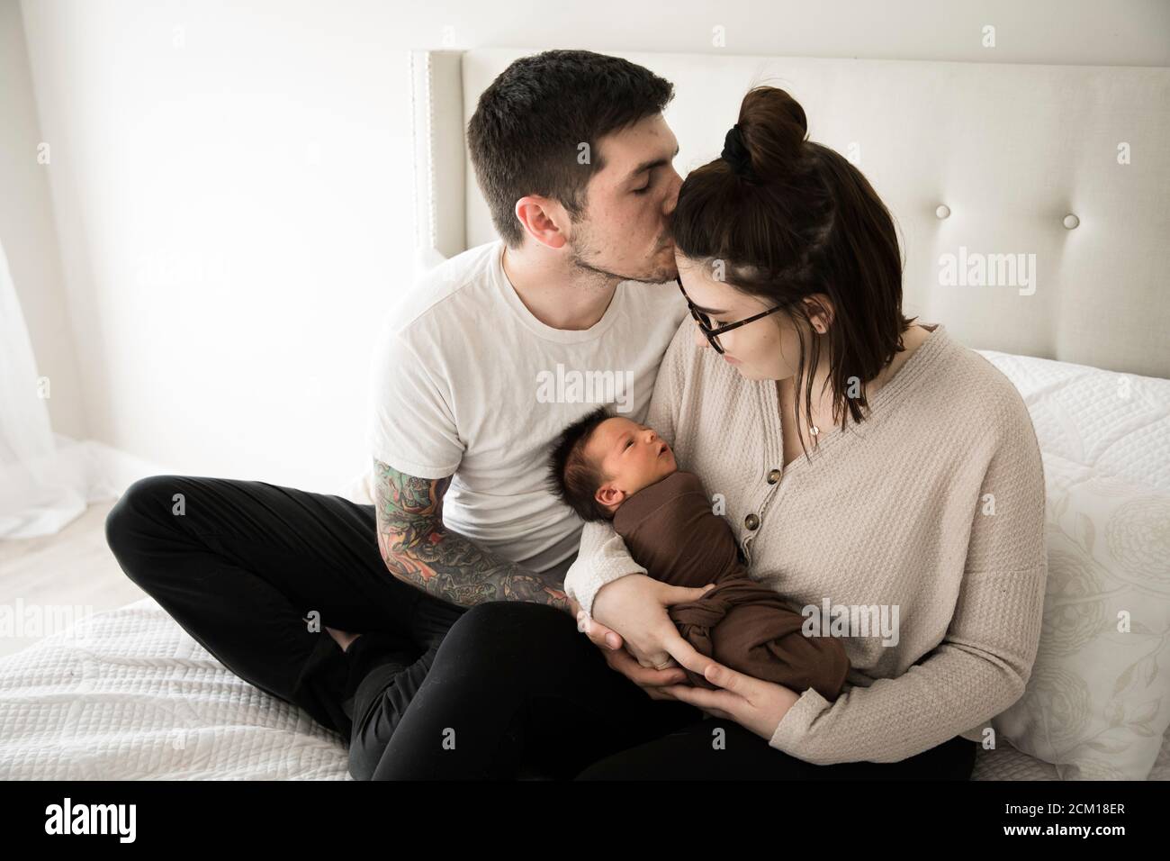 Tattooed Millennial Dad Kisses mamma mentre tiene il loro neonato Foto Stock