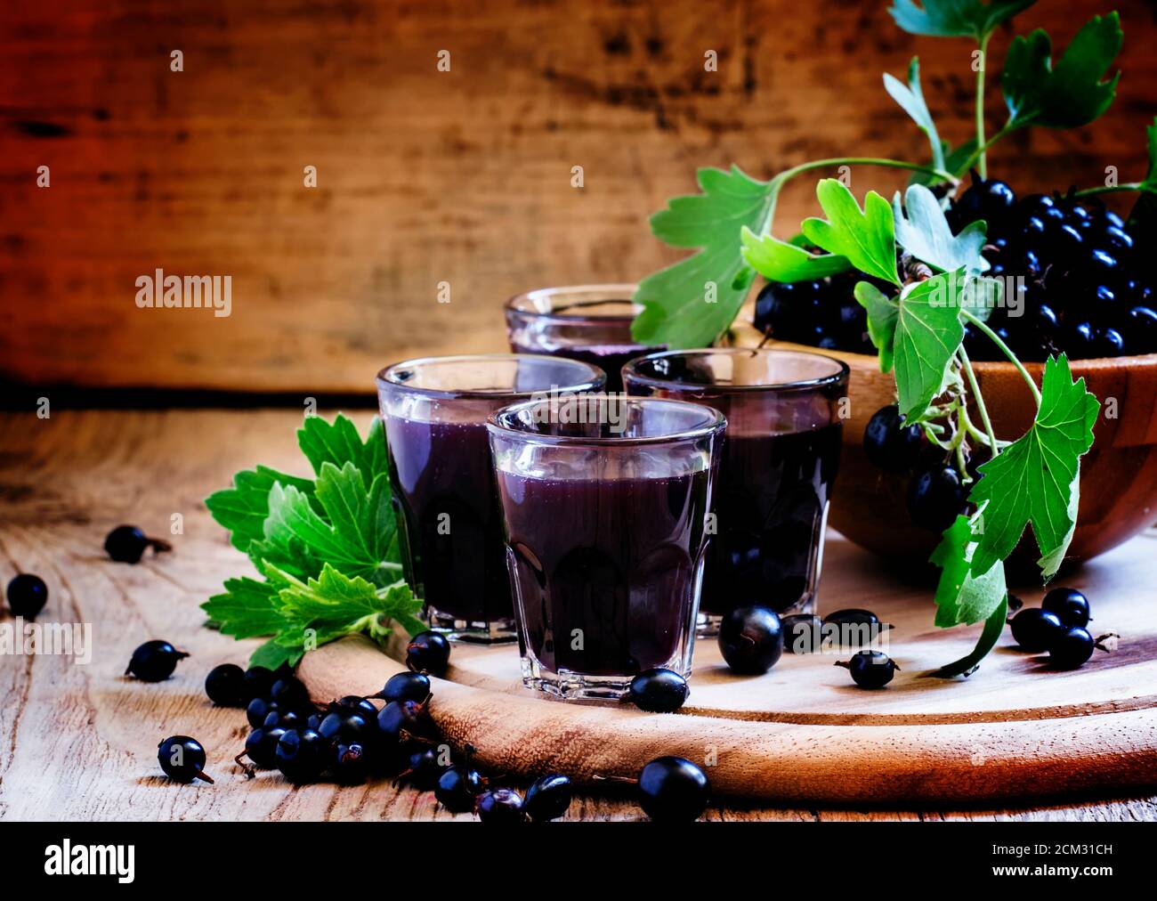 Liquore fatto in casa a base di ribes nero e frutti di bosco freschi, fondo in legno vintage, fuoco selettivo Foto Stock