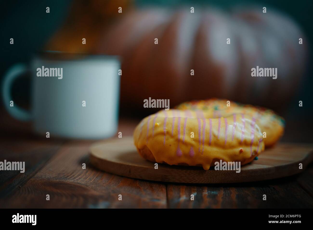 Ciambelle dolci con glassa di banana e cospargere su un vassoio di legno UNA grande zucca rotonda e una tazza bianca sullo sfondo. Composizione autunnale per cartoline. Foto Stock