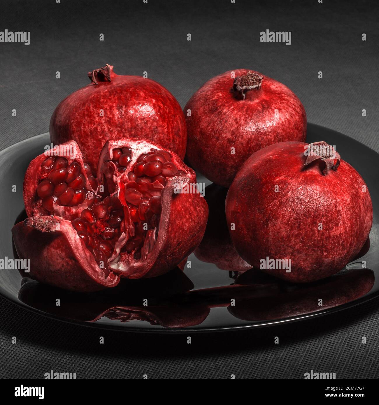 Melograno su un piatto nero, su un fone grigio neutro Foto Stock