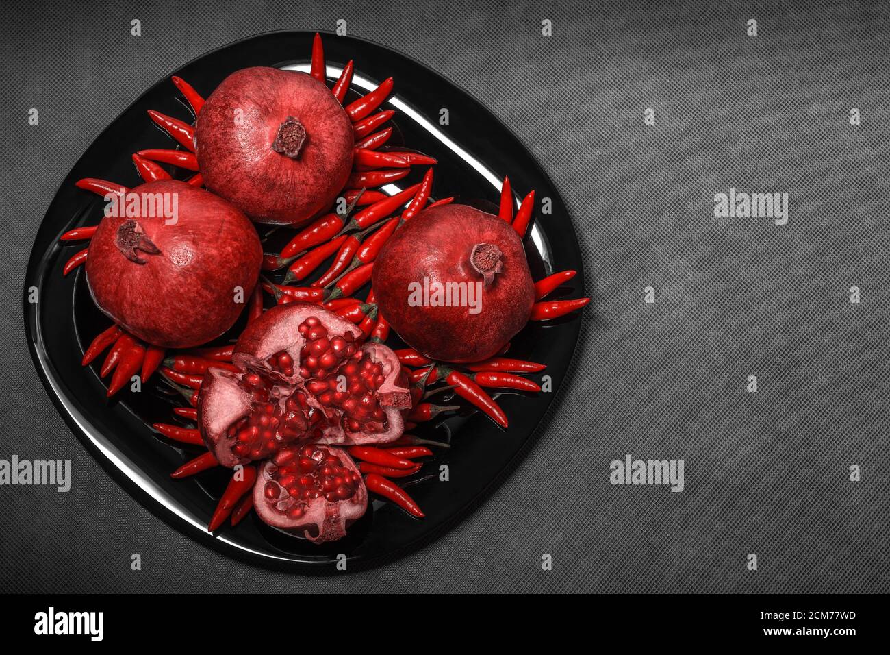Melograno disposto su un piatto nero, su fondo grigio neutro, orizzontale Foto Stock