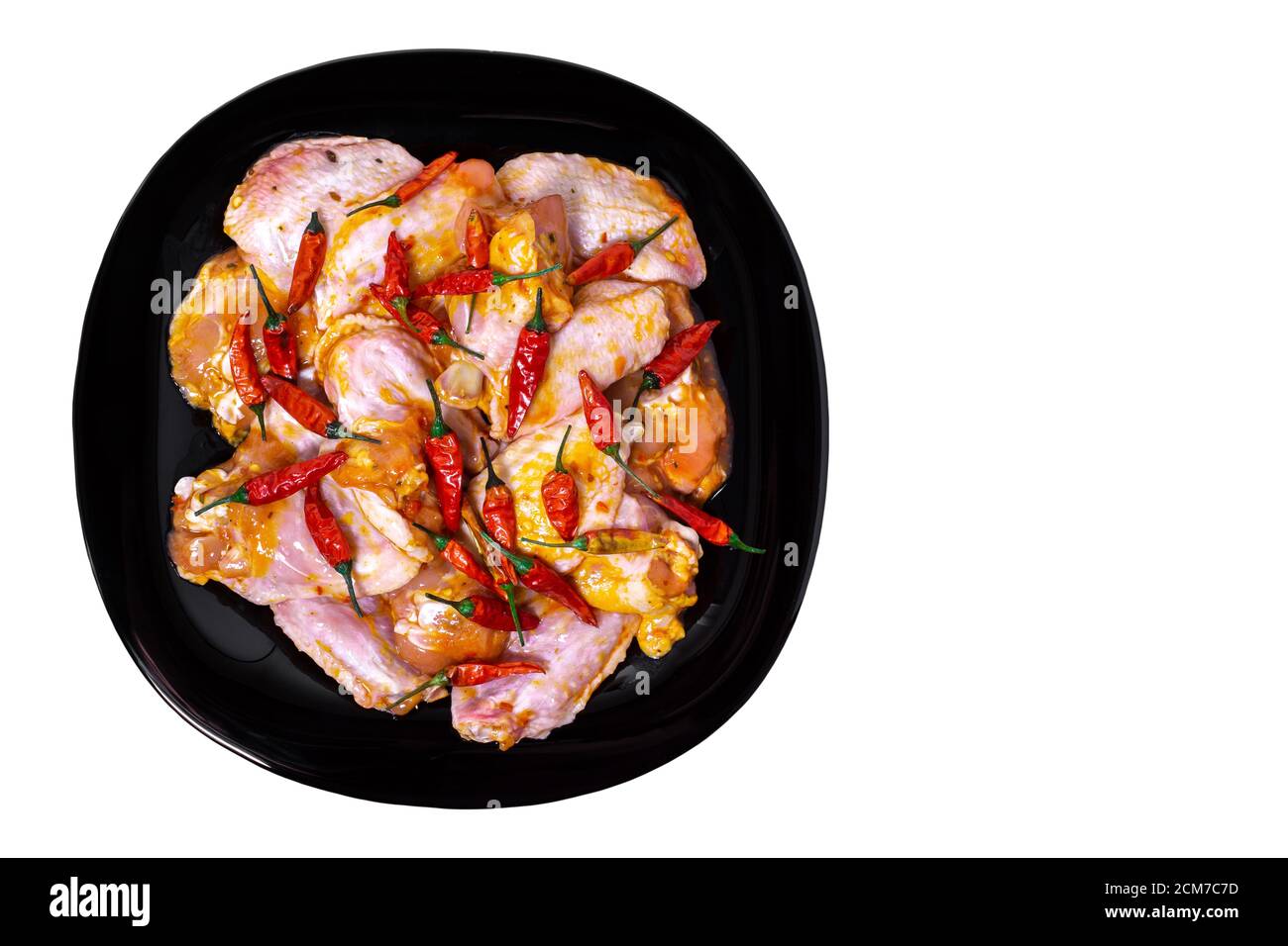 Ali di pollo crudo in una marinata con spezie su un piatto nero, un sacco di peperone rosso caldo, vista dall'alto, isolato, concetto di cibo Foto Stock