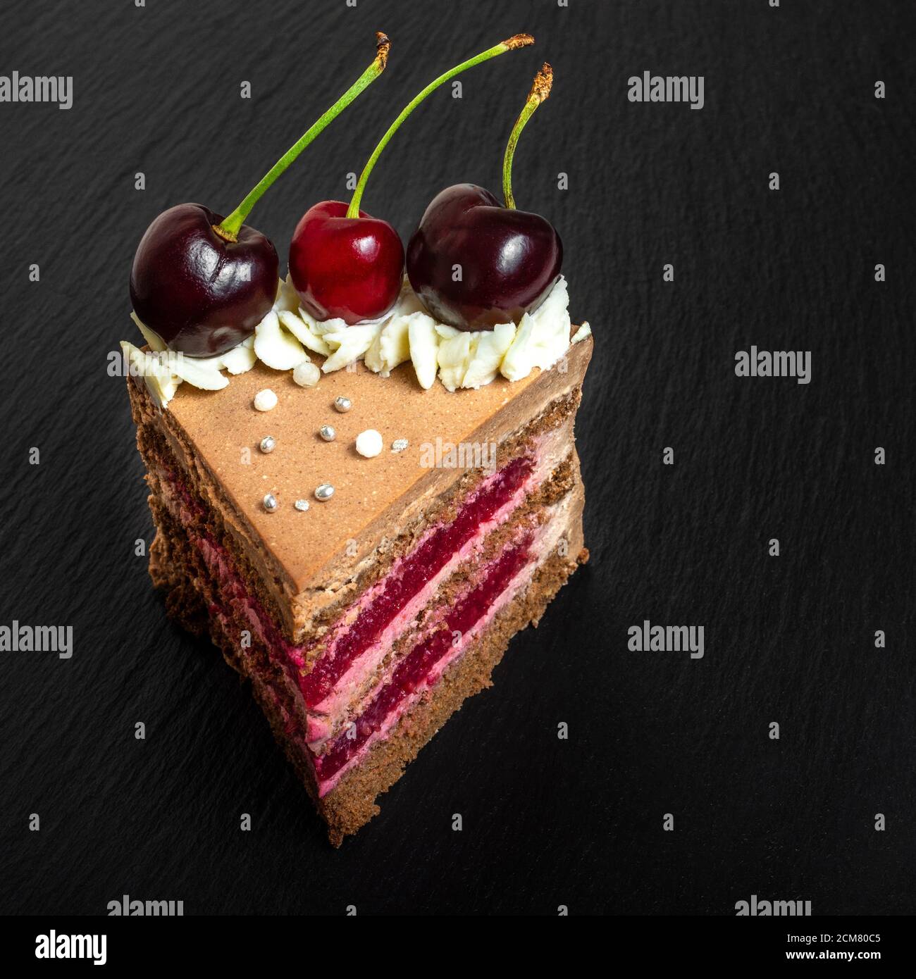 Dettaglio su una fetta di torta della Foresta Nera, o tradizionale torta austriaca schwarzwald dal cioccolato fondente e ciliegie acide su tavola nera Foto Stock