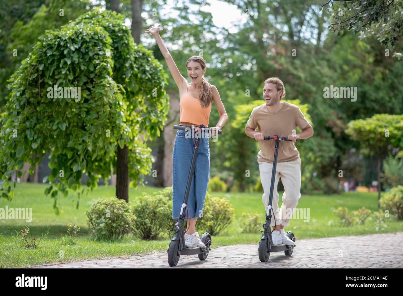 Una giovane coppia che guida gli scooter nel parco e si sente incredibile Foto Stock