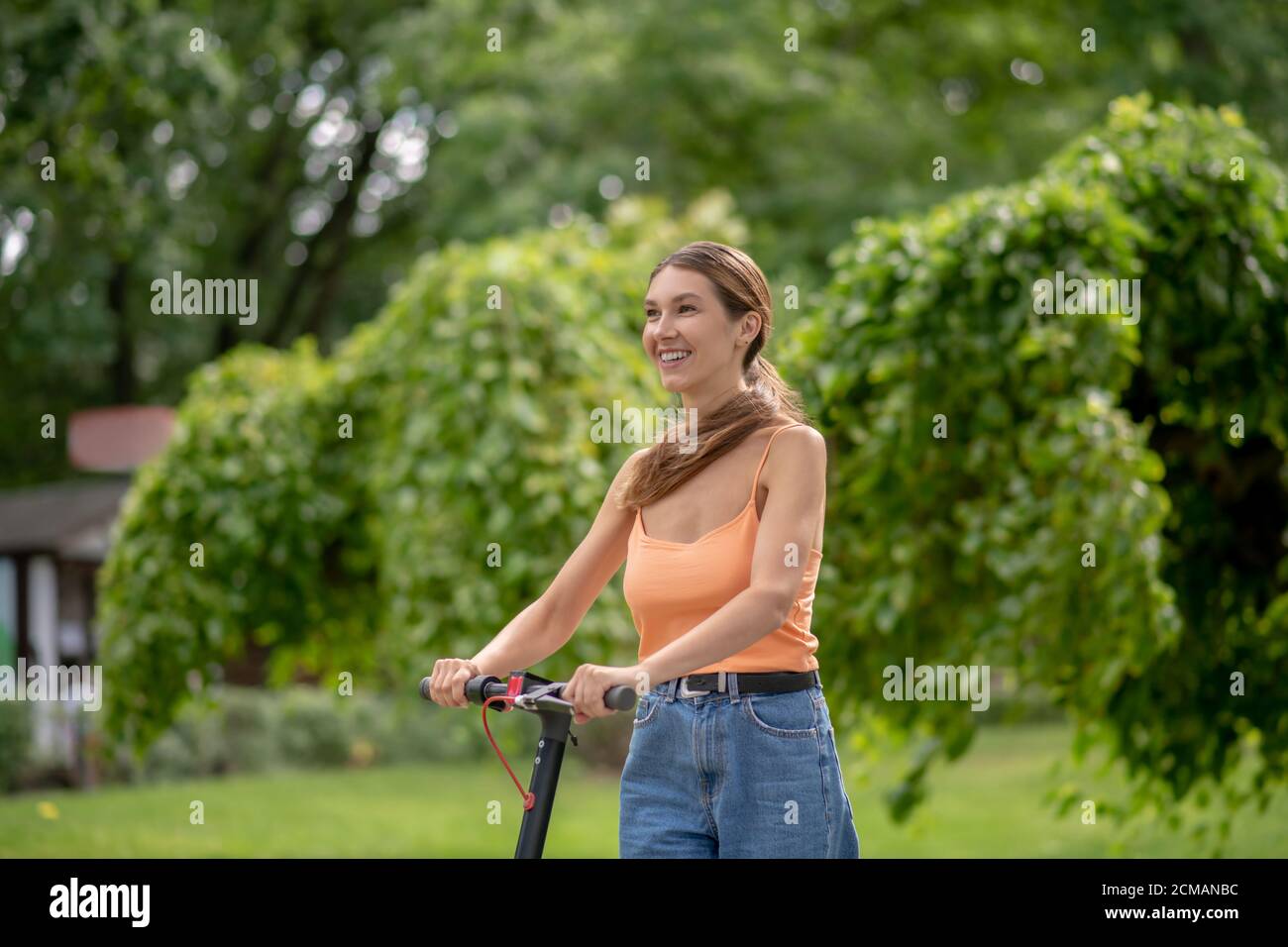 Giovane ragazza in cima arancione che cavalca uno scooter e sorride Foto Stock