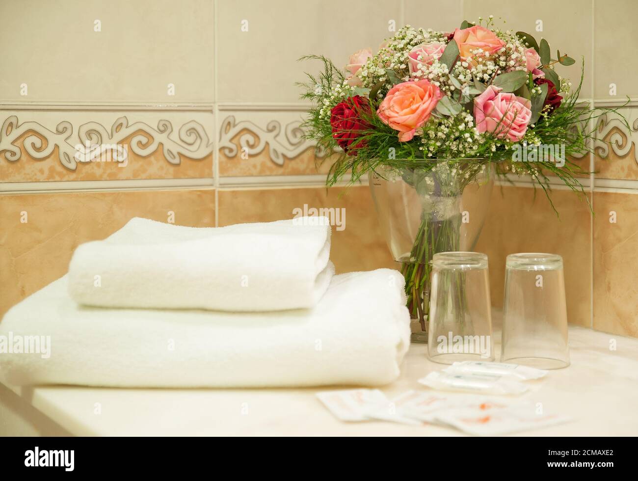 Il bagno rustico dell'hotel è dotato di un set di asciugamani bianchi, bicchieri di base, sapone e un bouquet di rose, accessori adatti per il pernottamento e la colazione Foto Stock