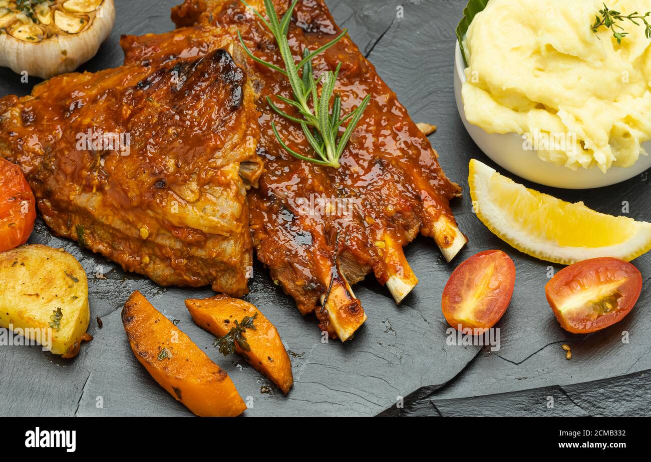 Costolette di maiale arrosto con purè di patate e pomodori arrosto su fondo piatto di pietra nera. Foto Stock