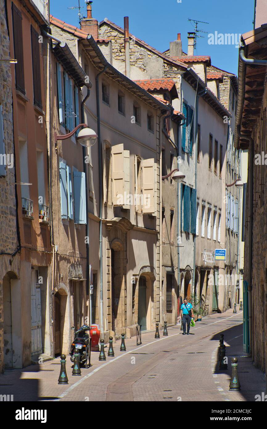 Una strada laterale illuminata dal sole che mostra i classici vecchi vani porta, le finestre e le persiane nella vecchia città di Millau, Aveyron, Francia. Una sola persona cammina in lontananza. Foto Stock