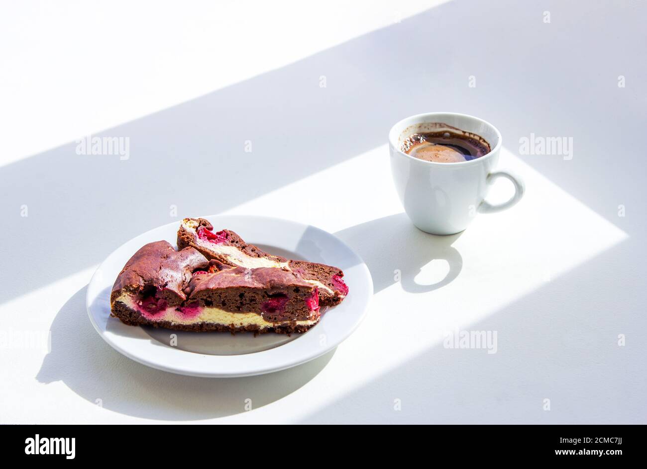 Tazza di caffè e torta brownie fatta in casa con formaggio casolare e ciliegie sul tavolo. Colazione al mattino soleggiato. Foto Stock