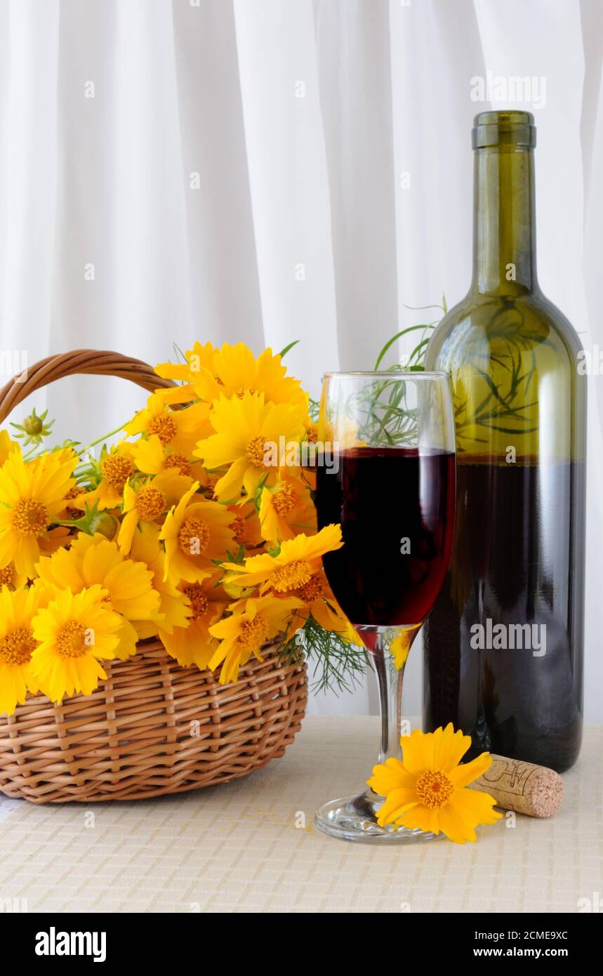 Una bottiglia di vino rosato con un bicchiere e giallo fiori in un cesto Foto Stock