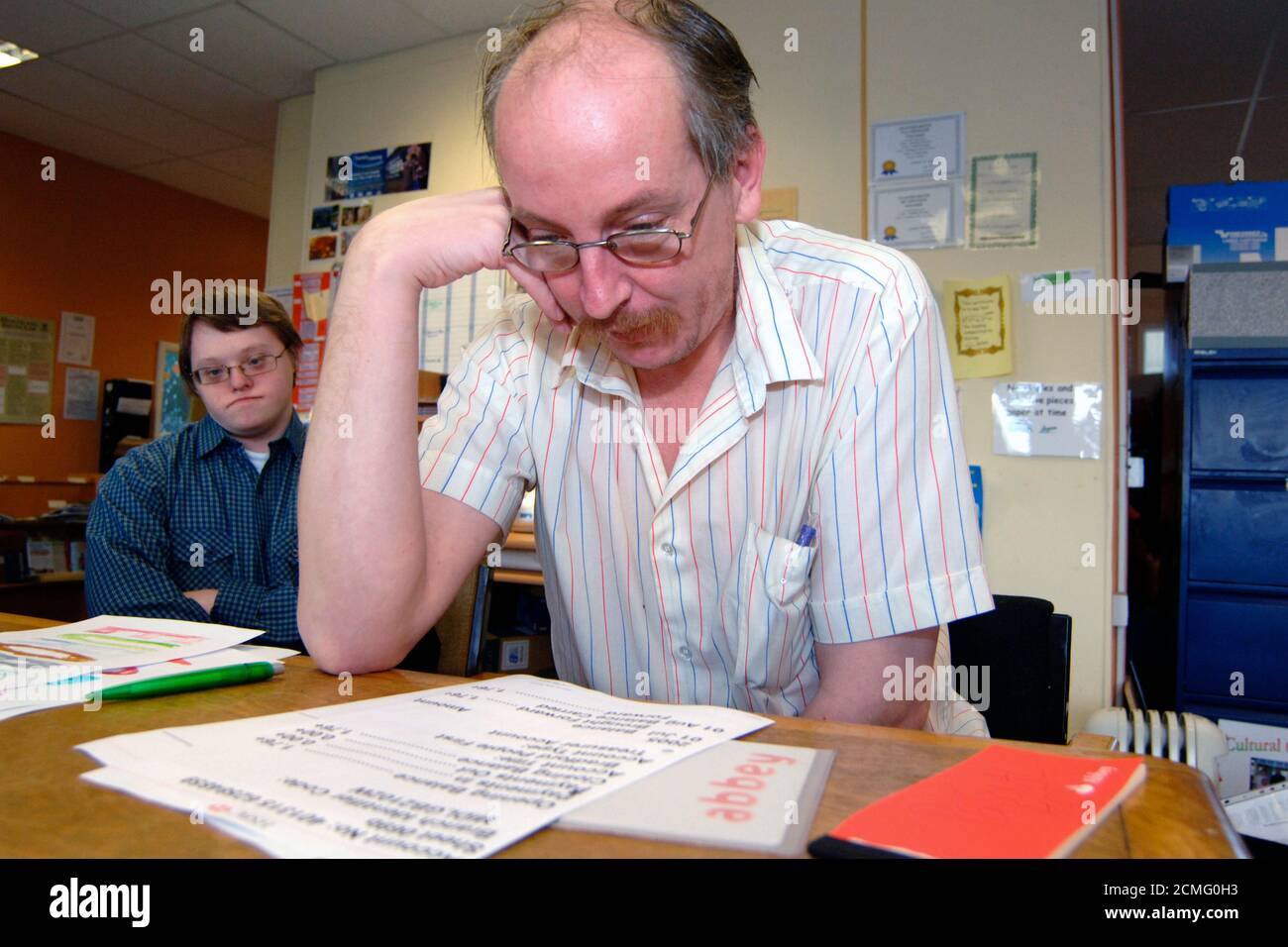 Uomo con disabilità di apprendimento che legge grande stampa dichiarazione bancaria; centro di comunità; Bradford; Yorkshire UK Foto Stock