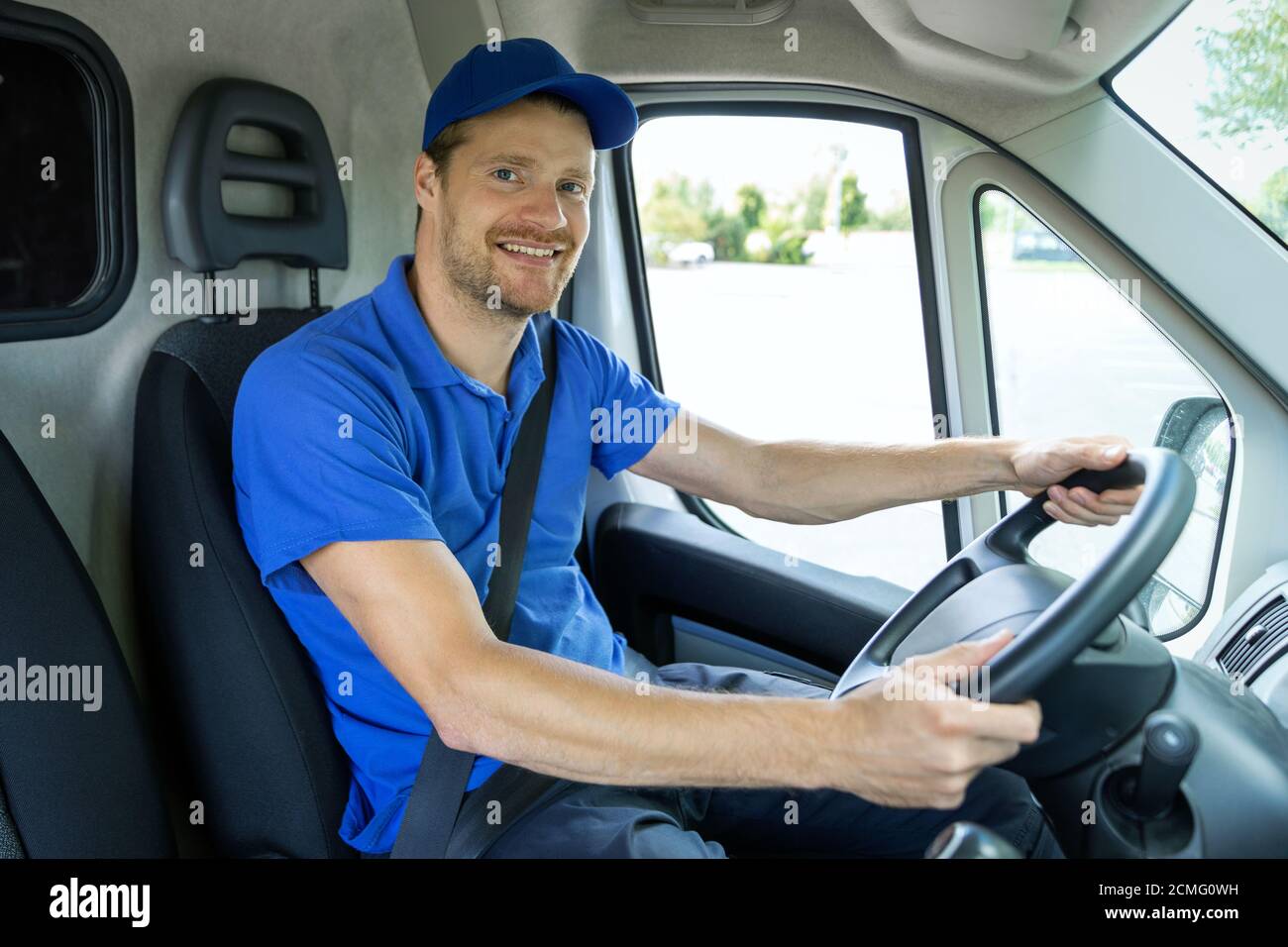 servizi di trasporto - giovane autista di sesso maschile in uniforme blu che guida un furgone. sorridendo alla macchina fotografica Foto Stock