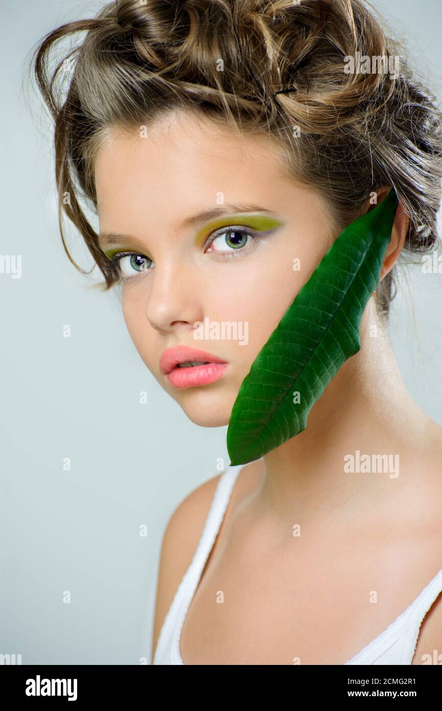 Ritratto di bellezza di una giovane ragazza con trucco verde brillante e una foglia fresca sul viso. Foto Stock