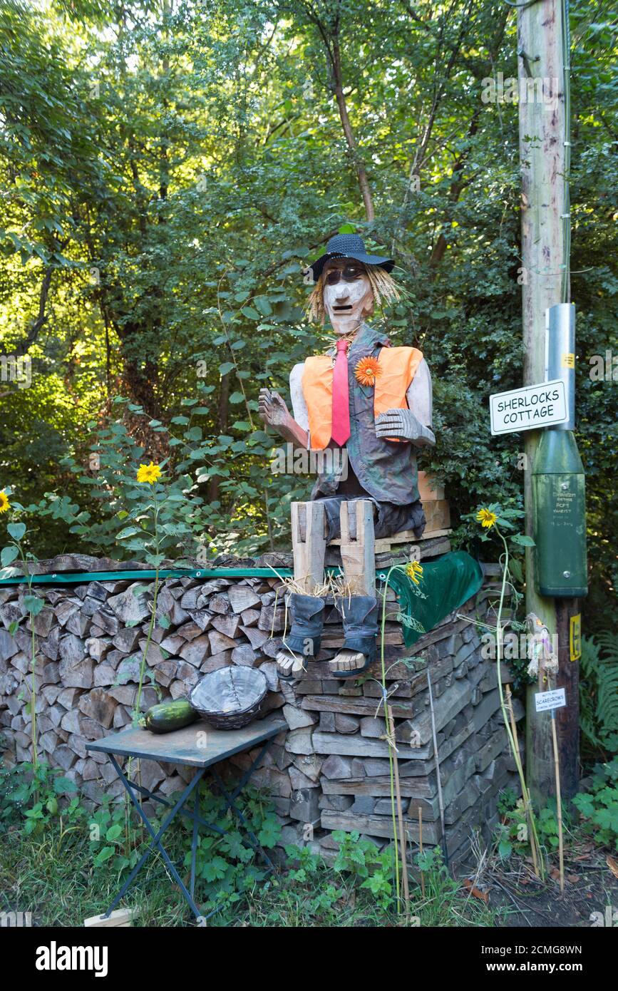 Vista insolita a grandezza naturale sulla corsia di campagna vestita con cappottatura e seduta eremita scarecrow indossando divisa intelligente nel giardino di fronte vendere verdure Foto Stock
