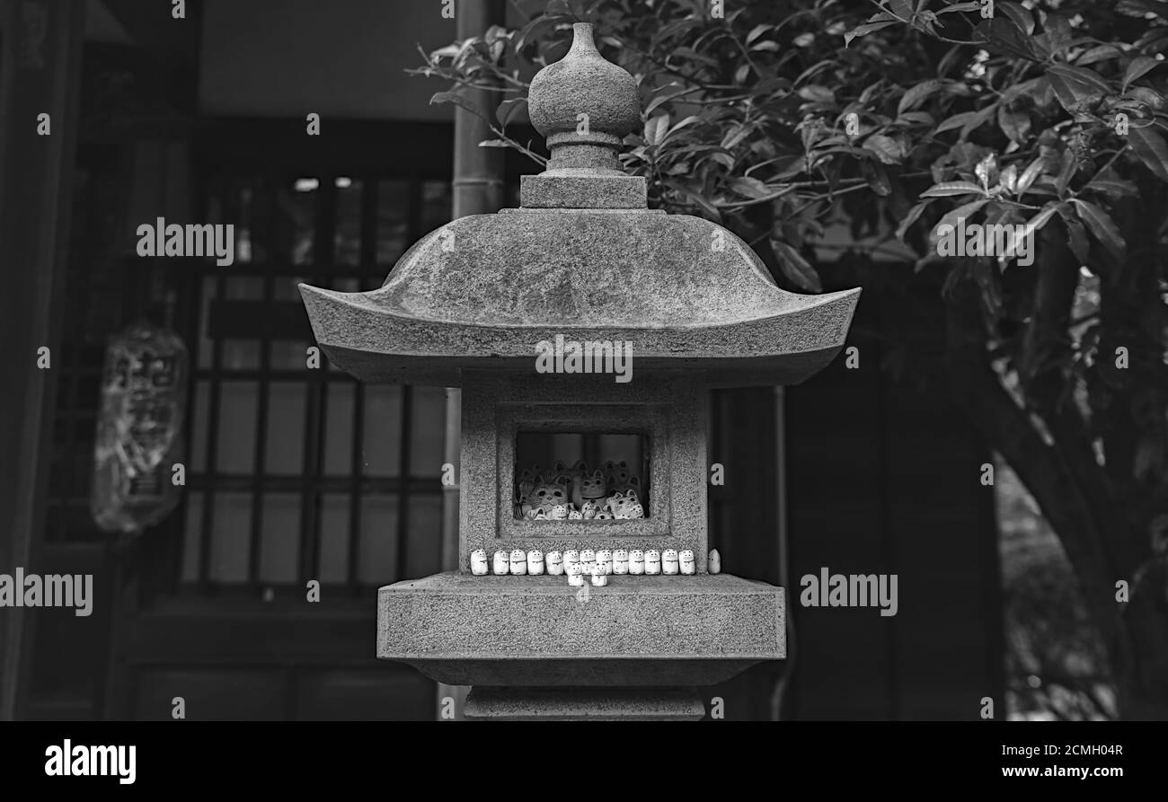 Vista delle statuette giapponesi maneki-neko 'beckoning Cat' poste in e su una lanterna di pietra, al Tempio Gotokuji a Tokyo Foto Stock