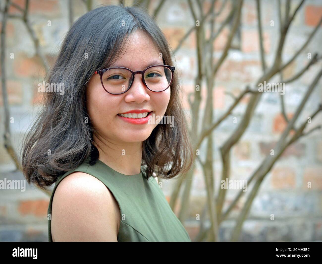 Sorridente giovane donna d'affari vietnamita con occhiali pone all'aperto per la macchina fotografica. Foto Stock