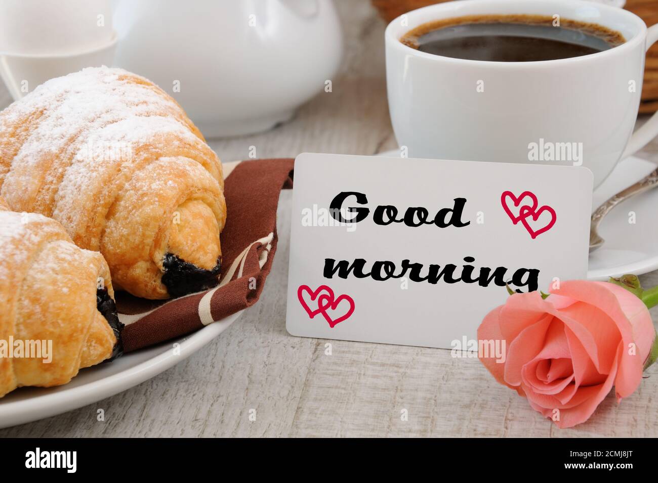 Prima colazione a base di croissant, tazza di caffè fresco del mattino con ripieno di cioccolato E una carta con un buon augurio Foto Stock