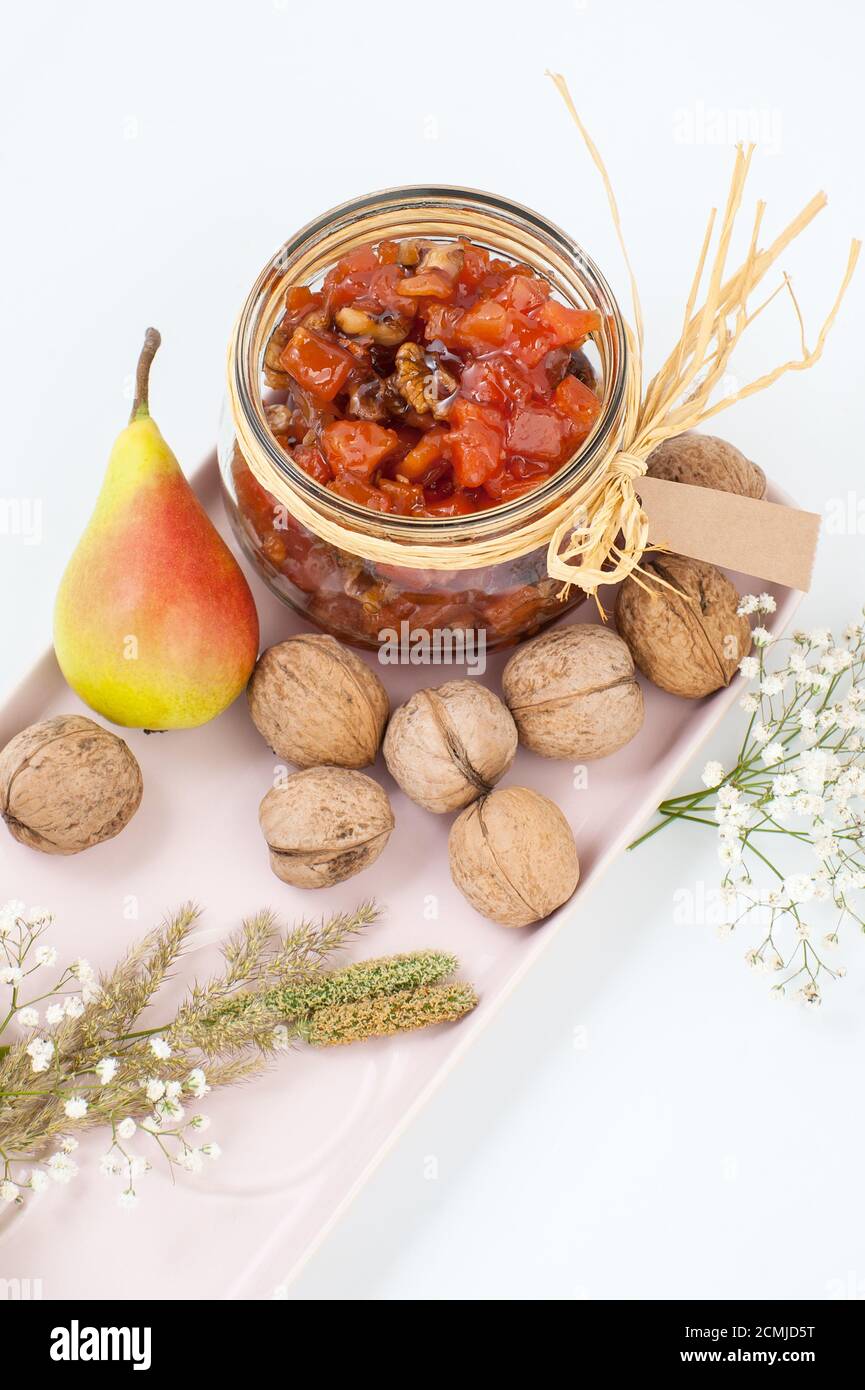 Marmellata di pere, pere e noci su un vassoio rosa chiaro su uno sfondo bianco primo piano. Foto Stock