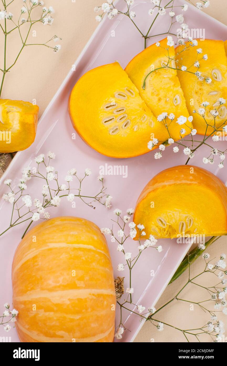 Fette di zucca giovane fresca su un piatto rosa chiaro su uno sfondo arancione pastello. Foto Stock