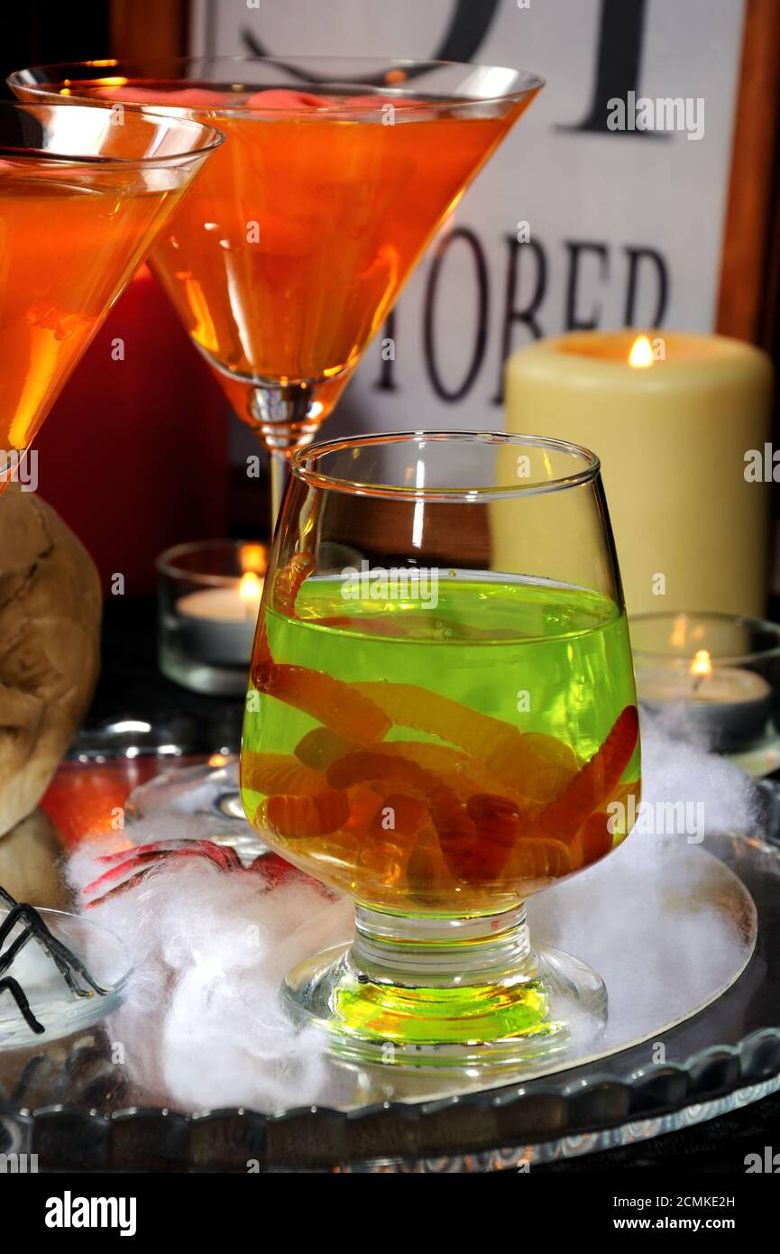 Bicchiere con una bevanda verde con vermi su un tavolo In onore di Halloween tra gli altri cocktail Foto Stock