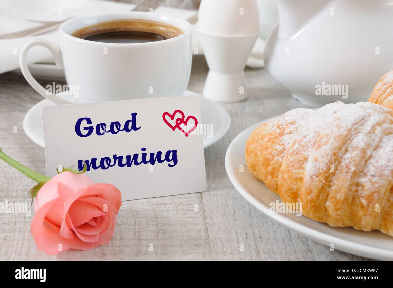 Prima colazione a base di croissant, tazza di caffè fresco del mattino con ripieno di cioccolato E una carta con un buon augurio Foto Stock