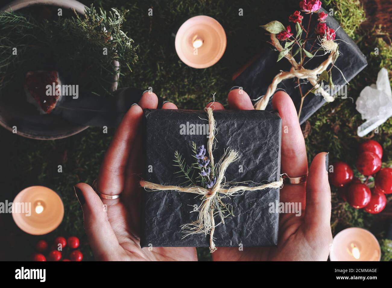 Yule solstice invernale (Natale) piatto a tema posa di mani femminili contiene una scatola regalo nera avvolta in filato e fiori nelle sue mani Foto Stock