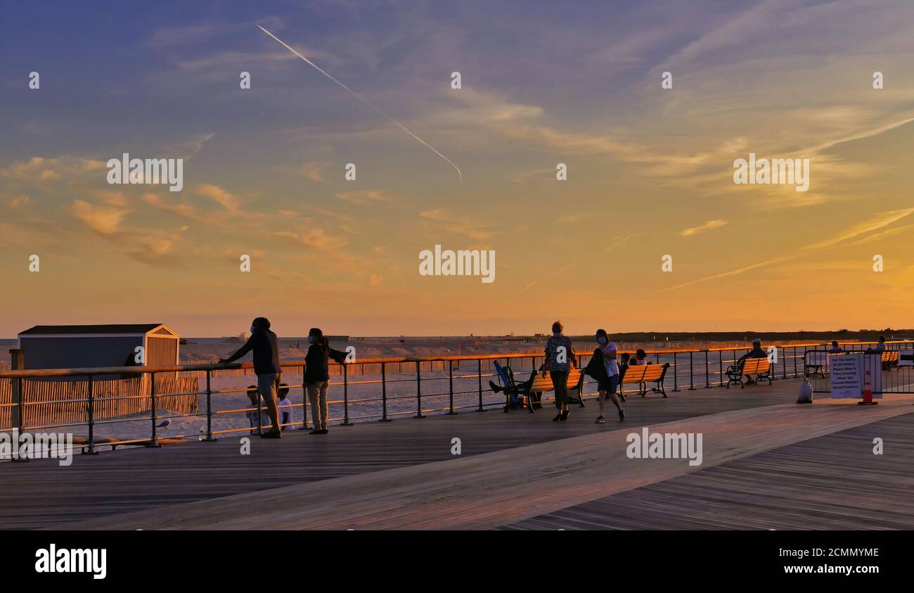 Persone che camminano lungo la passeggiata a bordo al tramonto. Foto di alta qualità. Rosso, cielo arancione e nuvole Foto Stock