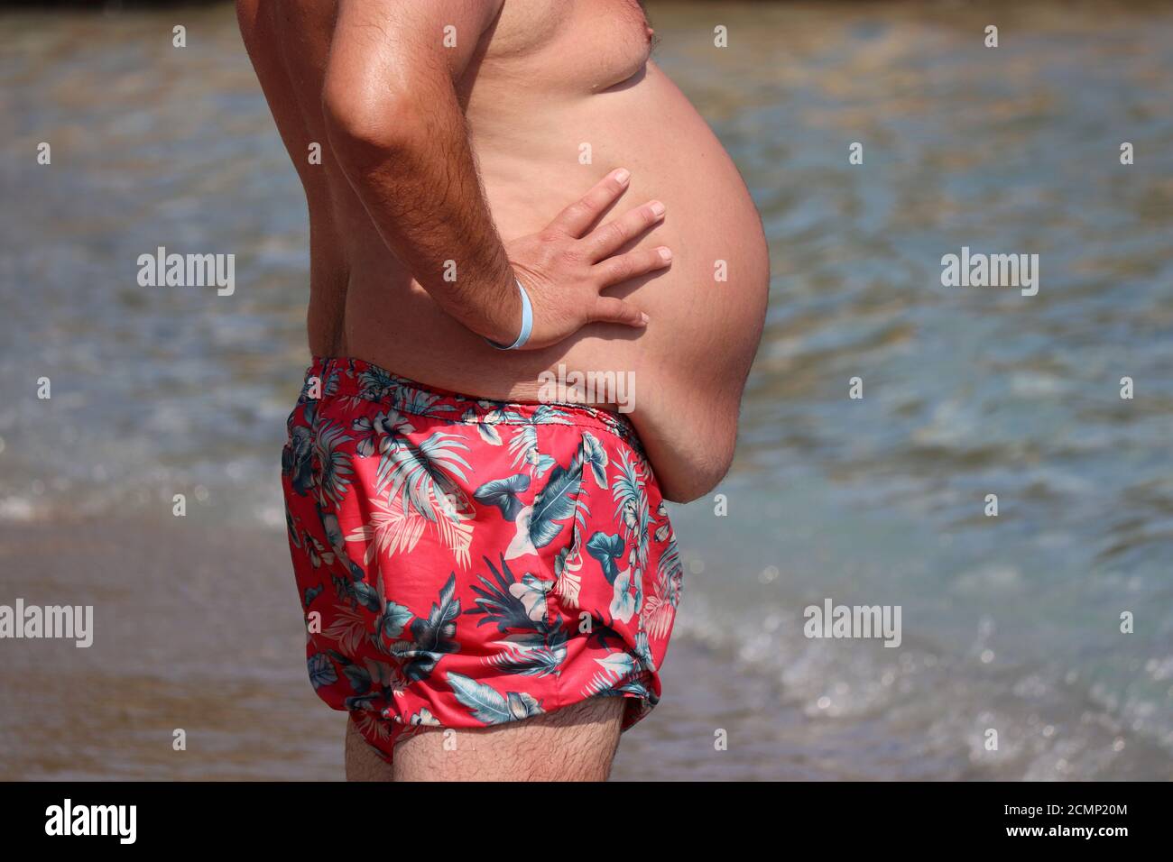 Uomo con pancia grassa in piedi su una spiaggia. Sovrappeso e concetto di obesità Foto Stock