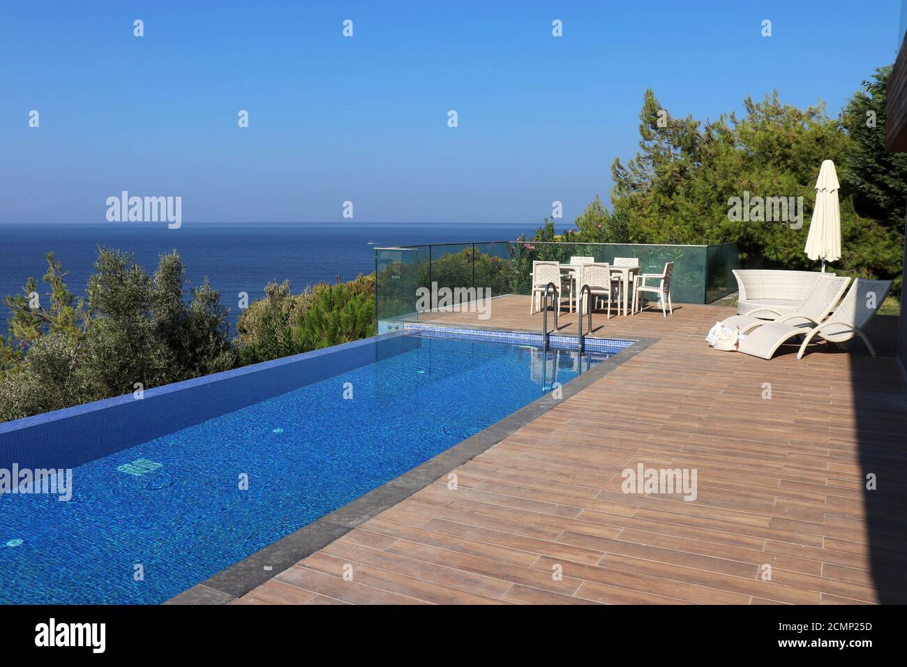 Piscina e area solarium sulla montagna con mare blu e alberi sullo sfondo. Villa di lusso sulla costa mediterranea, vacanza al mare Foto Stock