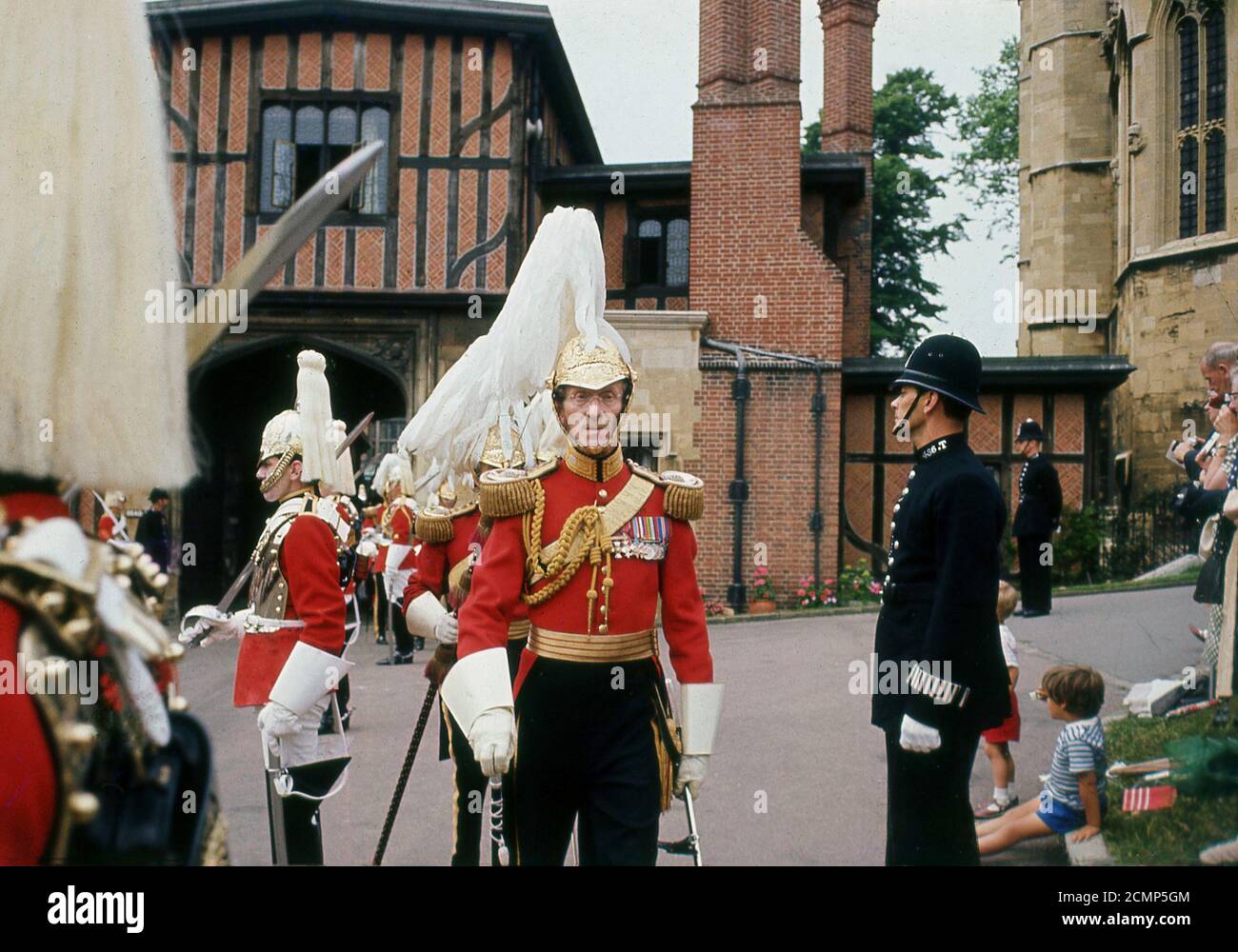 Anni '60, storico, fuori dal Castello di Windsor, le guardie del Queens indossano le loro tuniche di vestito rosso in dovere cerimoniale, con un poliziotto britannico anche in presenza. Dal 1660, il privilegio di sorvegliare il Sovrano appartiene alle truppe della famiglia o 'le guardie', che consiste di cinque reggimenti di fanteria - le guardie di Grenadier, Coldsteam, scozzesi, irlandesi e gallesi - e di due reggimenti della Cavalleria domestica - i Giardi di vita e i Blues e Royals. Foto Stock