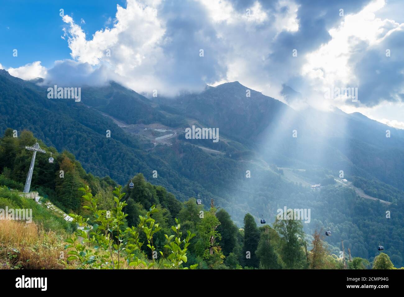 Un raggio di sole attraverso le nuvole illumina la funivia in montagna. Villaggio Olimpico di montagna, Krasnaya Polyana, Sochi, Russia. Foto Stock