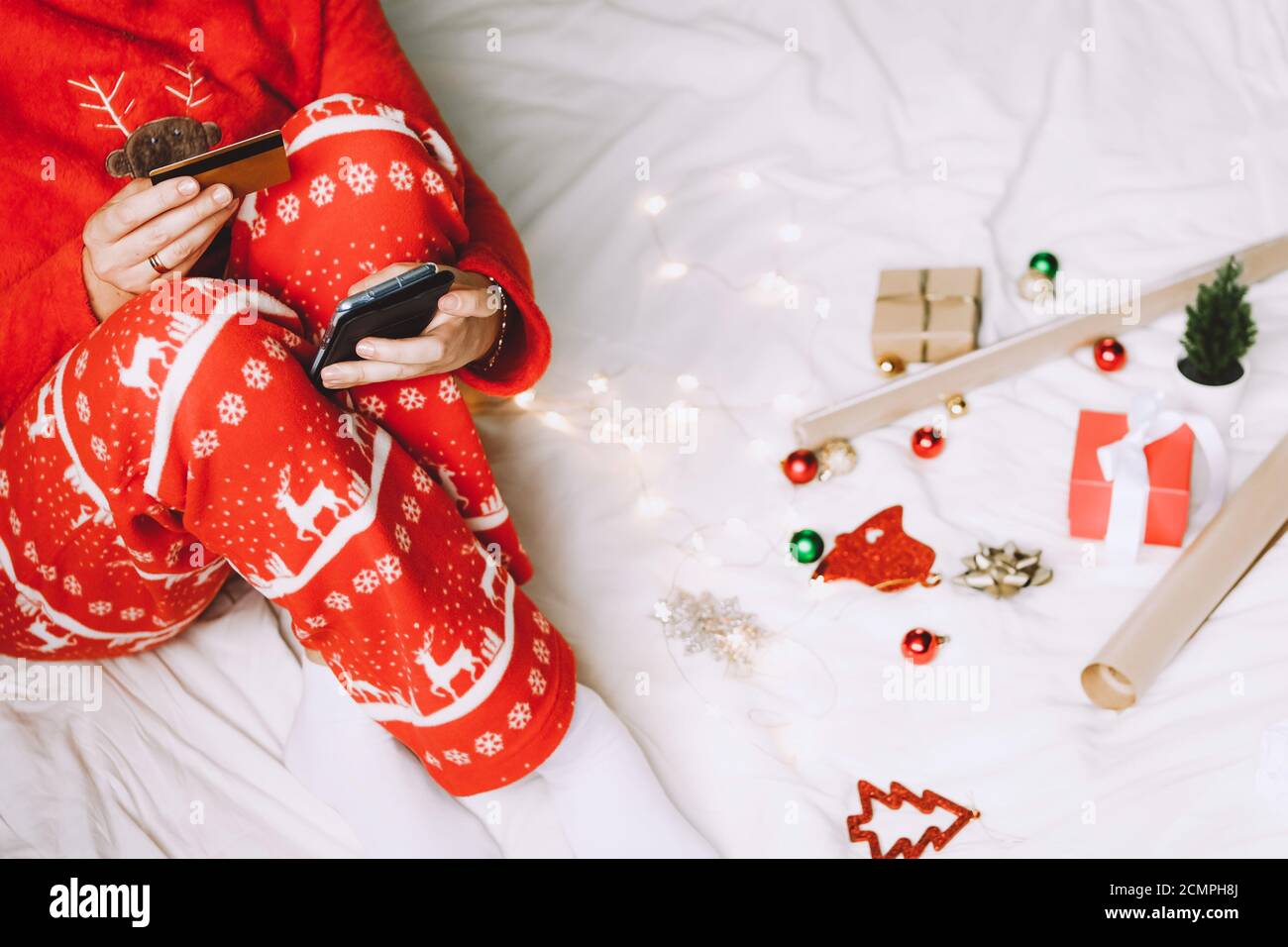 Donna che acquista in linea per i regali di Natale. Immagine ritagliata di una ragazza con telefono cellulare e carta di credito che prepara i regali di vacanza. Foto Stock