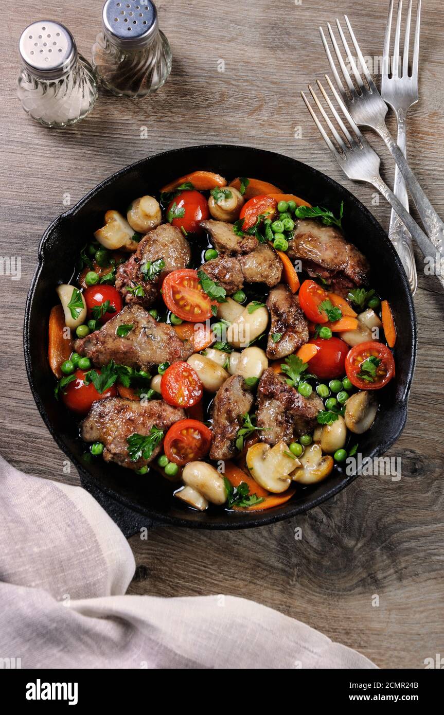 Fritti di fegato di pollo con verdura contorno di pomodori, carote, funghi piselli in padella Foto Stock