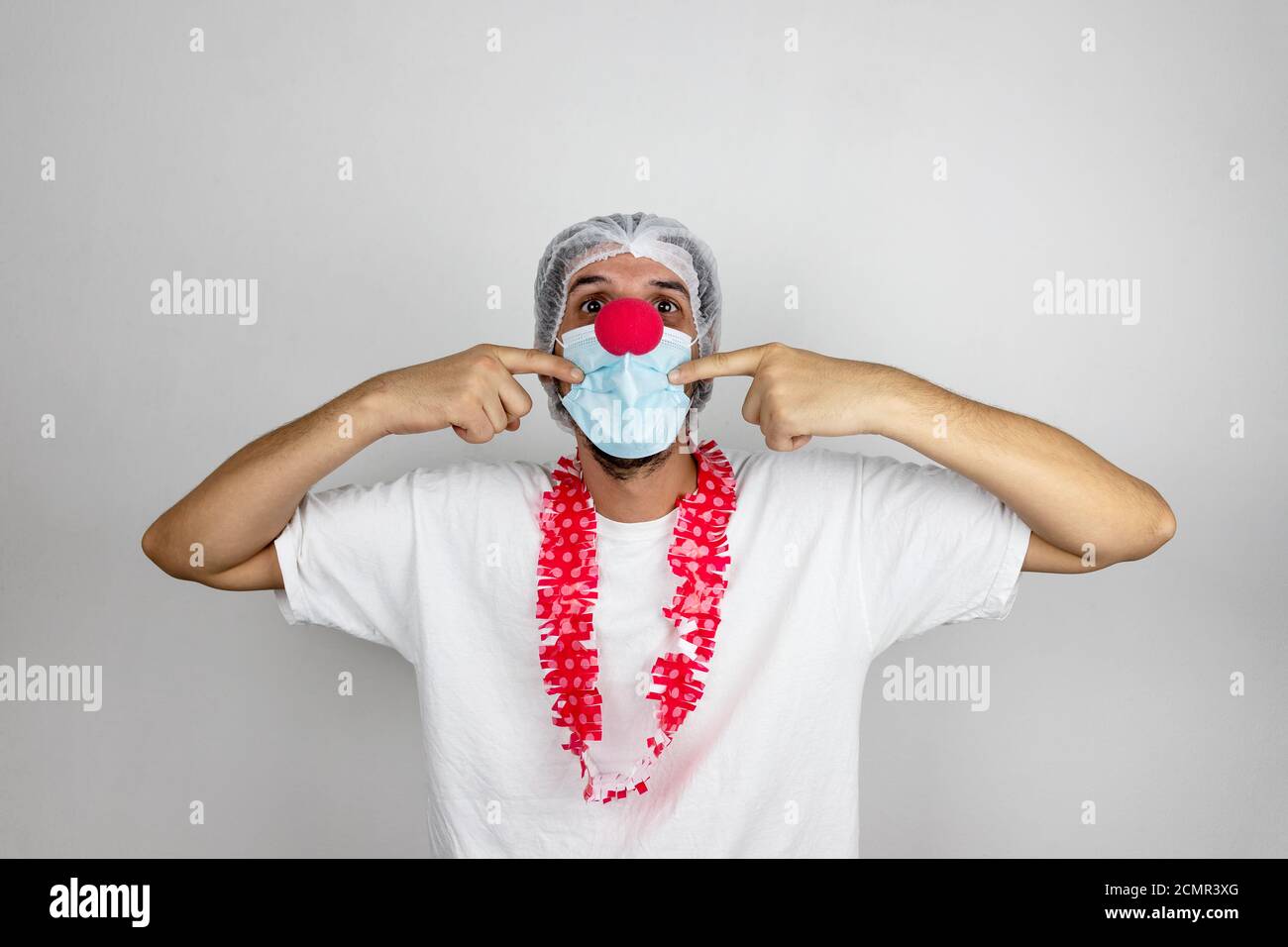 Giovane uomo che indossa indumenti protettivi e un naso pagliaccio, mostrando ad un paziente di sorridere. Medico positivo per i bambini. Infermiera divertente. Foto Stock