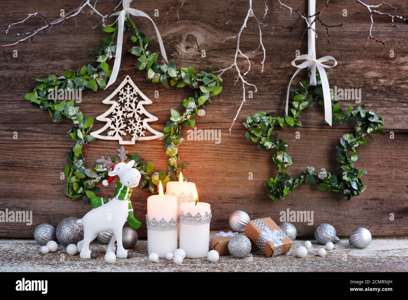 Composizione natalizia con candele, statuine di alce e decorazioni festive su sfondo ligneo. Biglietto d'auguri per Natale o Capodanno. Foto Stock