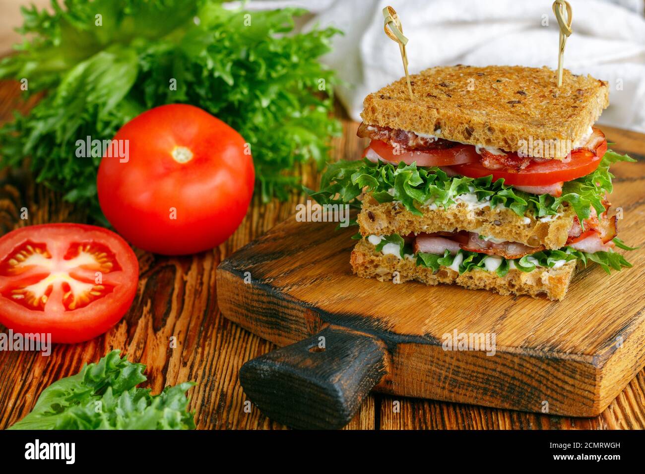 Deliziosi panini con insalata verde, prosciutto, pancetta, pomodori freschi e salsa su un tagliere di legno. Concetto di pranzo. Messa a fuoco selettiva Foto Stock