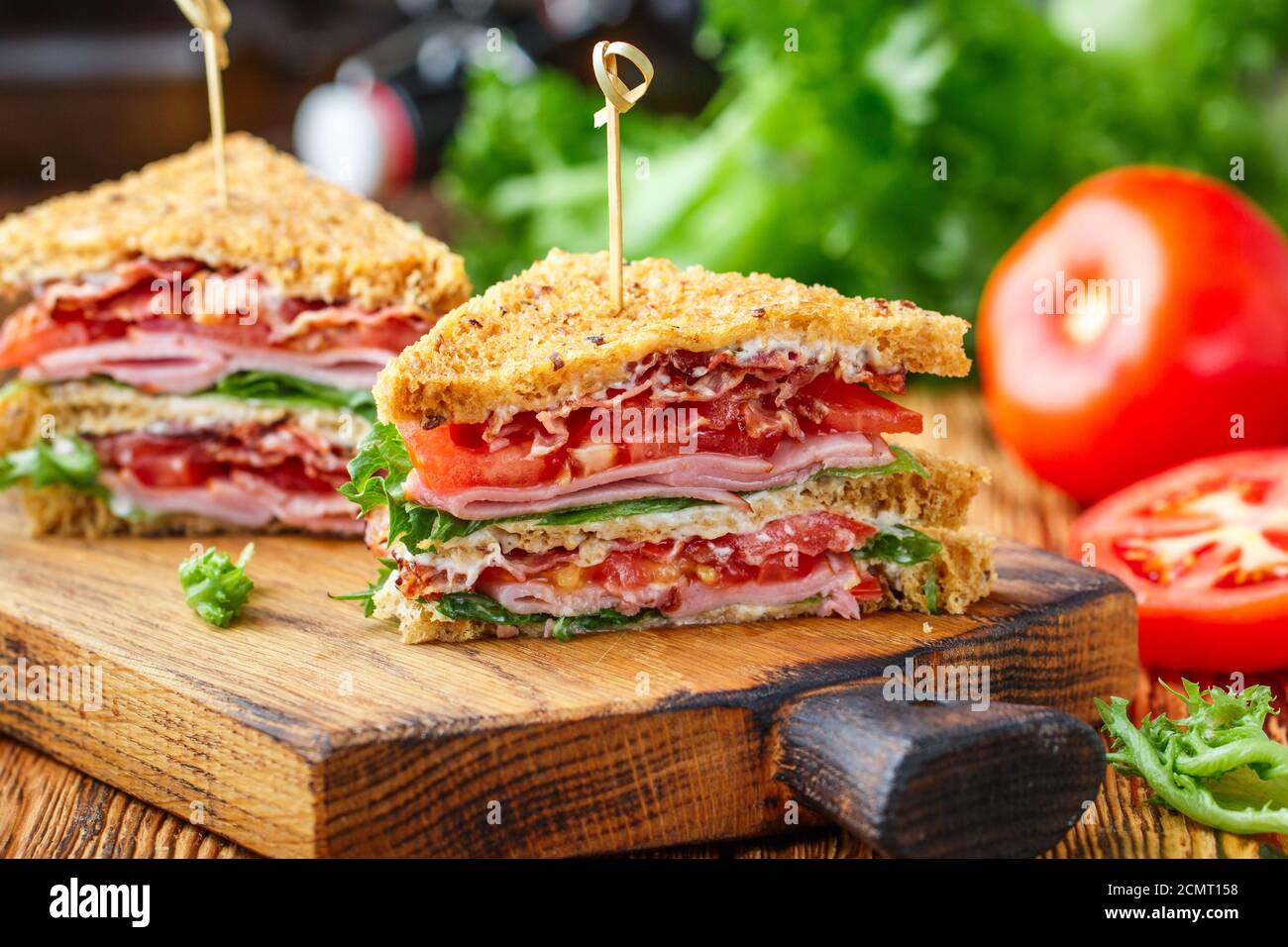 Deliziosi panini con insalata verde, prosciutto, pancetta, pomodori freschi e salsa su un tagliere di legno. Concetto di pranzo. Messa a fuoco selettiva Foto Stock