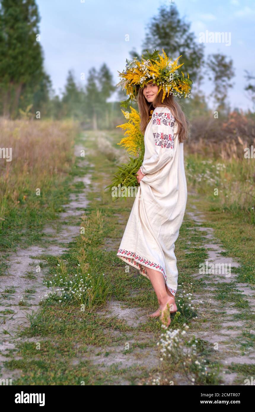 Bella donna in una corona di fiori selvatici e un antico abbigliamento nazionale camminando a piedi nudi sul percorso. Cultura Ucraina, vacanza di Ivana Kupala Foto Stock