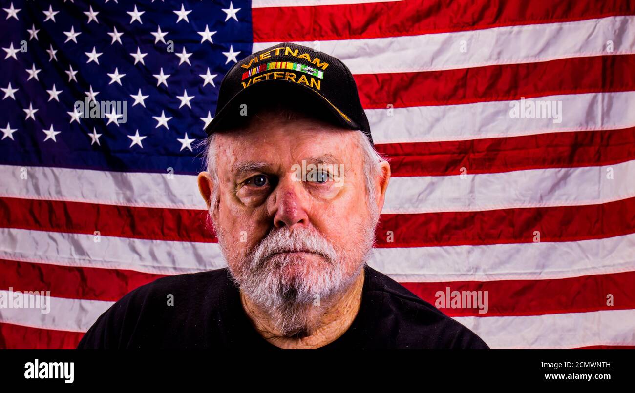 Vietnam Veteran con uno sguardo lontano con la bandiera americana sfondo Foto Stock