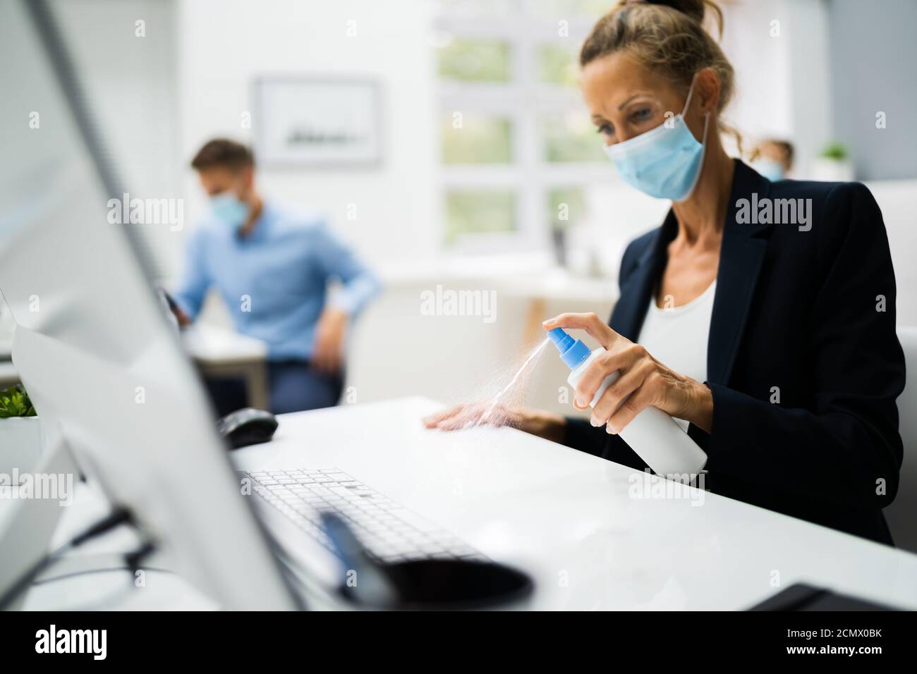 Donna pulizia scrivania in ufficio utilizzando disinfettante alcol Foto Stock