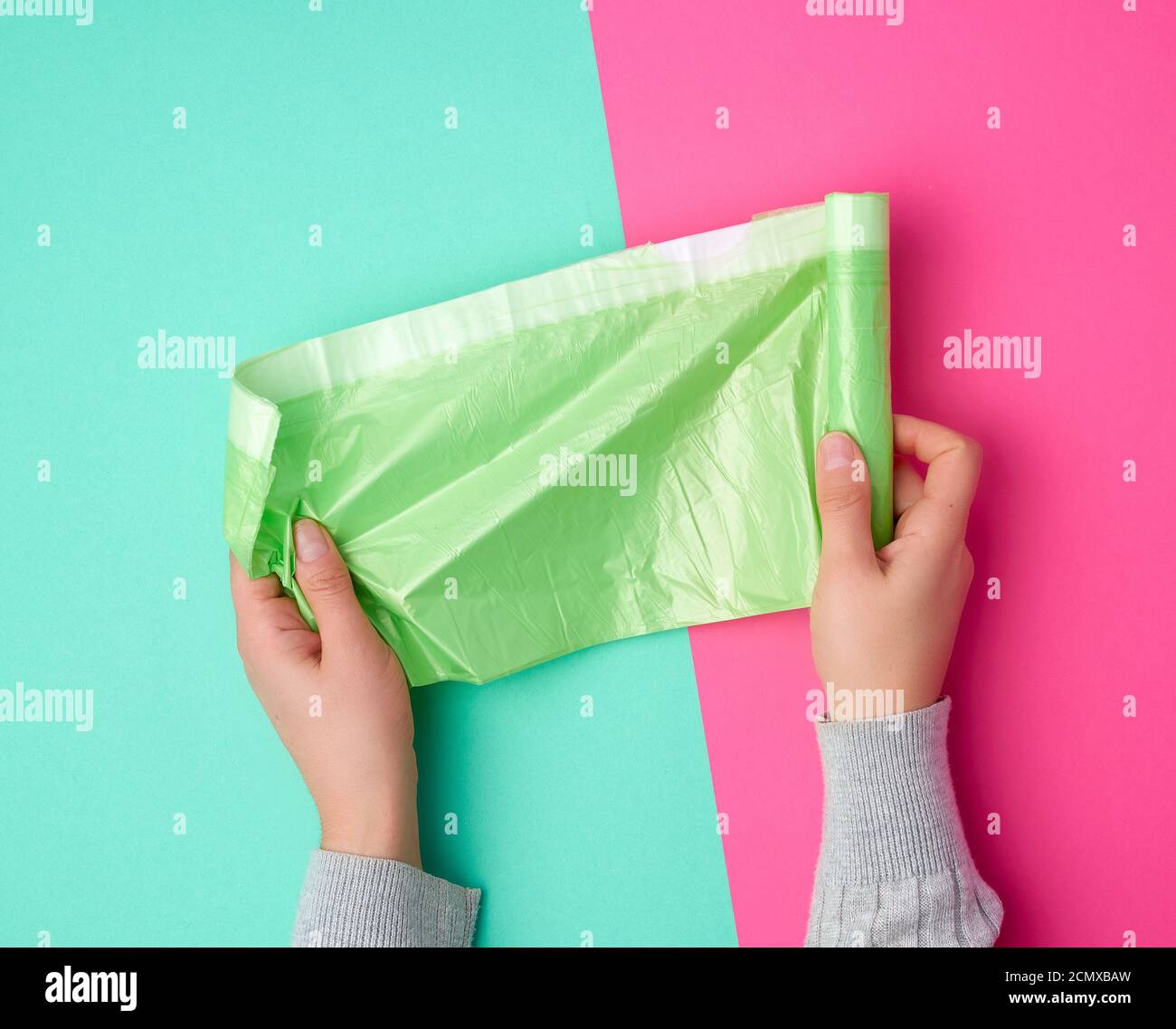 la mano femminile svolge un sacchetto di plastica verde per i rifiuti Foto Stock