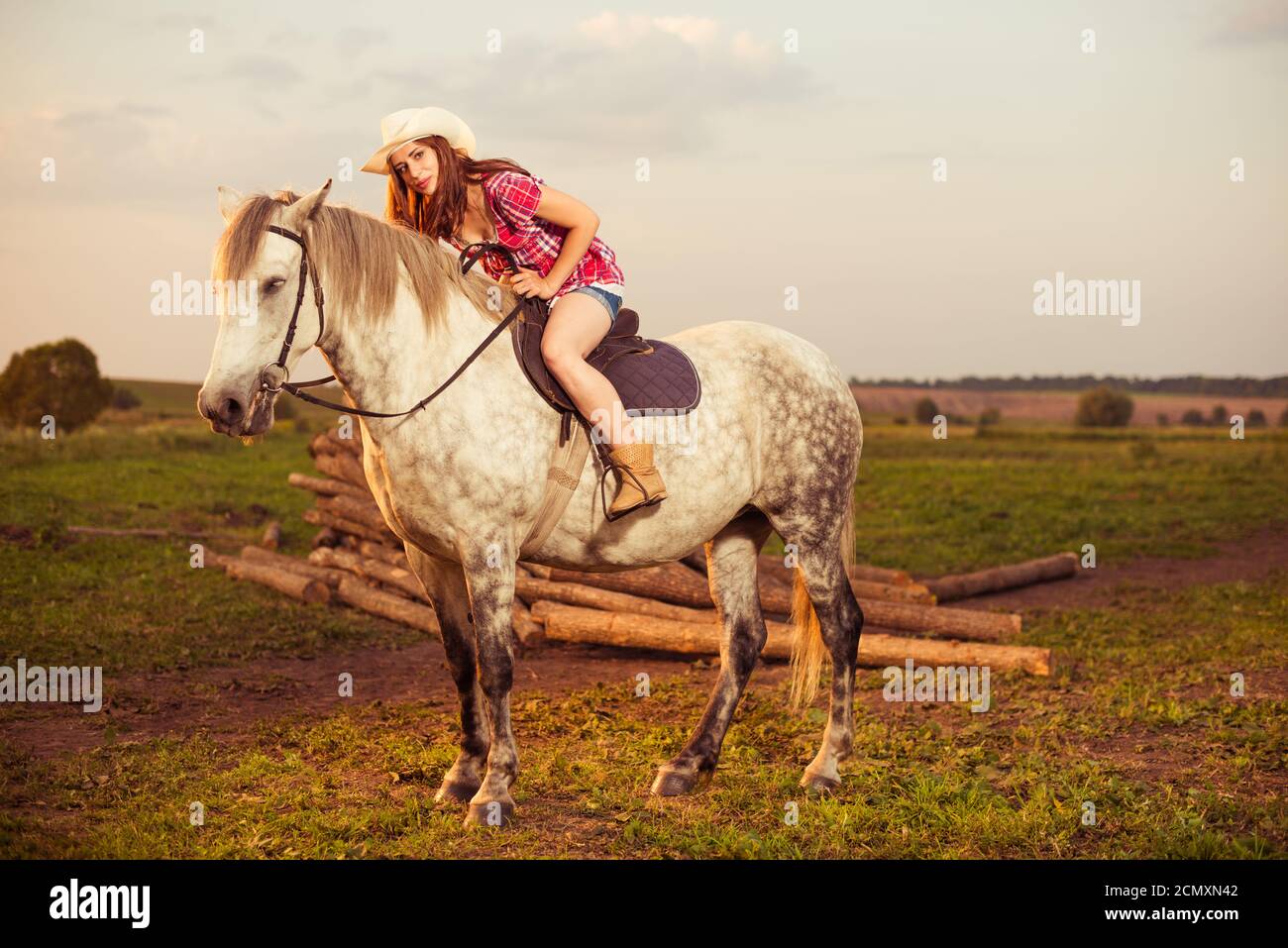 Giovane donna in cappello in estate fattoria tramonto cavalcare bianco cavallo Foto Stock