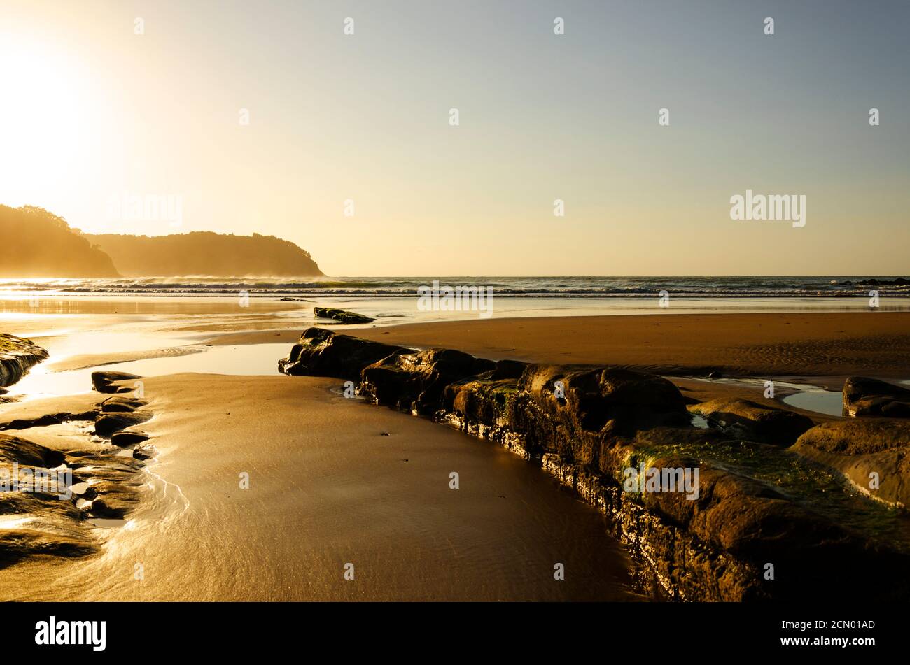 Spiaggia con una potente linea rocciosa e luce dorata Foto Stock