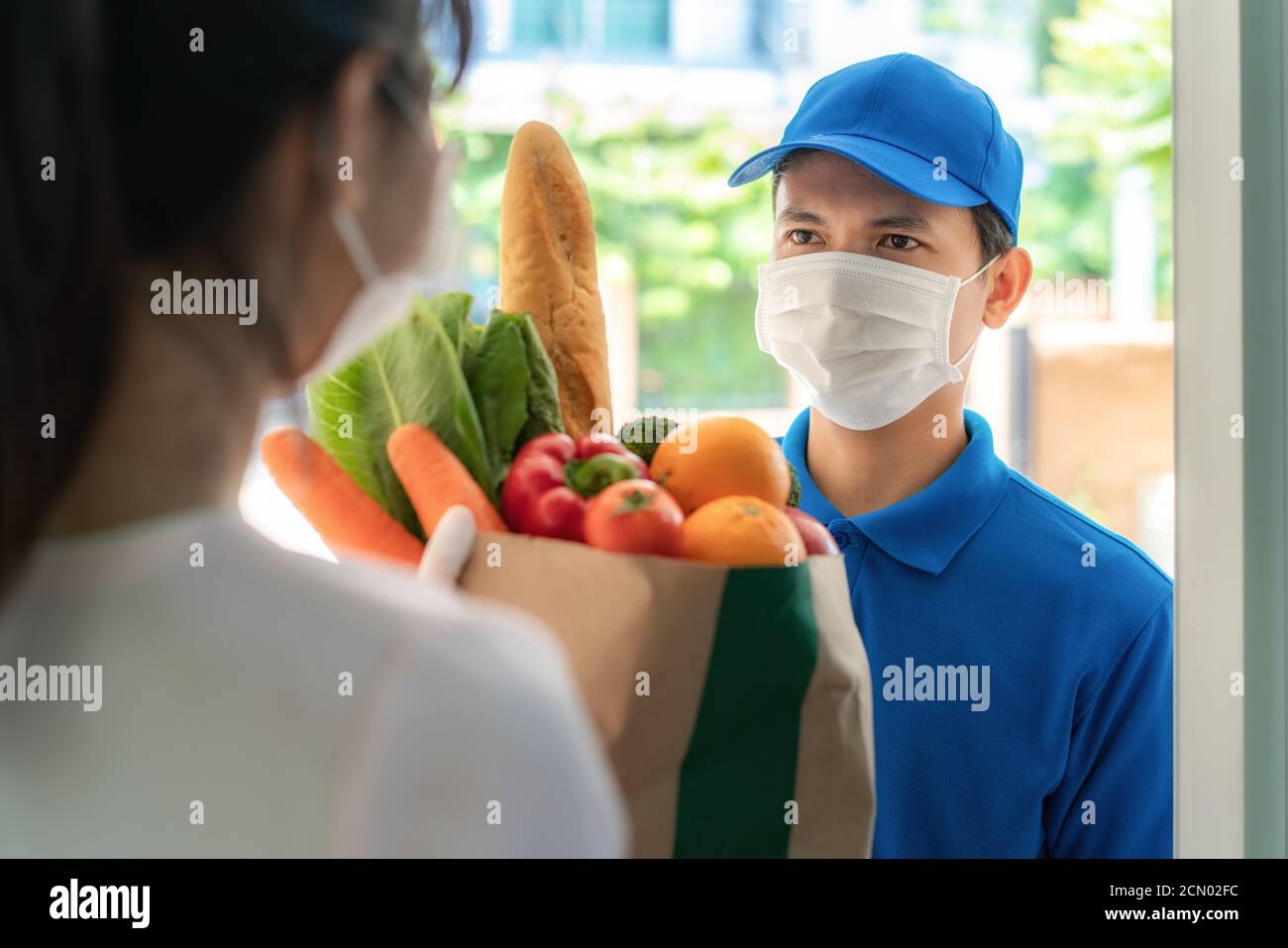 Asian consegna uomo che indossa maschera facciale e guanto con sacchetto di generi alimentari di cibo, frutta, verdura dare alla donna cliente di fronte alla casa durante il tempo o Foto Stock