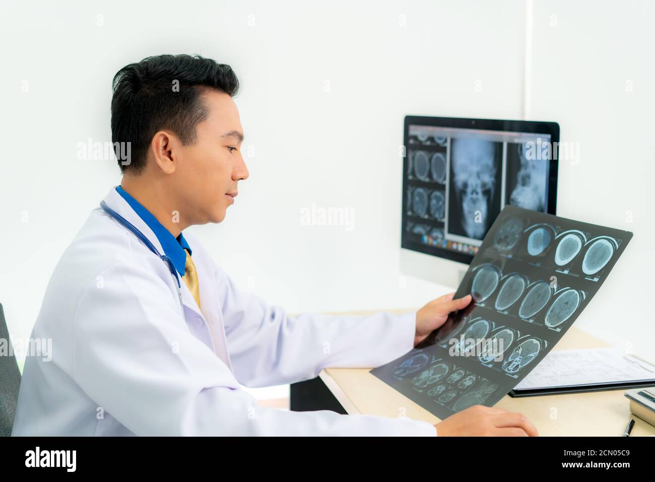Medico asiatico che tiene e guarda all'esame radiografico del cranio e del cervello del paziente in una clinica medica in ospedale. Foto Stock