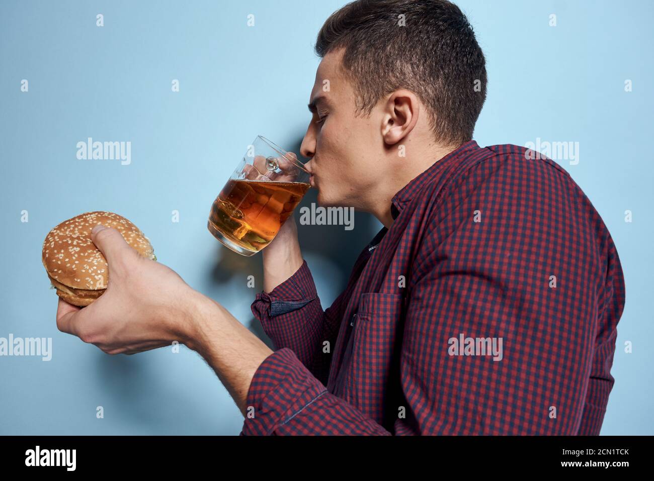 allegro ubriaco con tazza di birra e hamburger in mano dieta cibo stile di vita sfondo blu Foto Stock