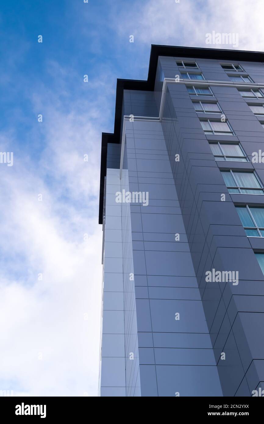 La parte superiore d'angolo di un alto e moderno edificio con pannelli in metallo grigio di vari colori. C'è un cielo blu con nuvole bianche sullo sfondo. Foto Stock