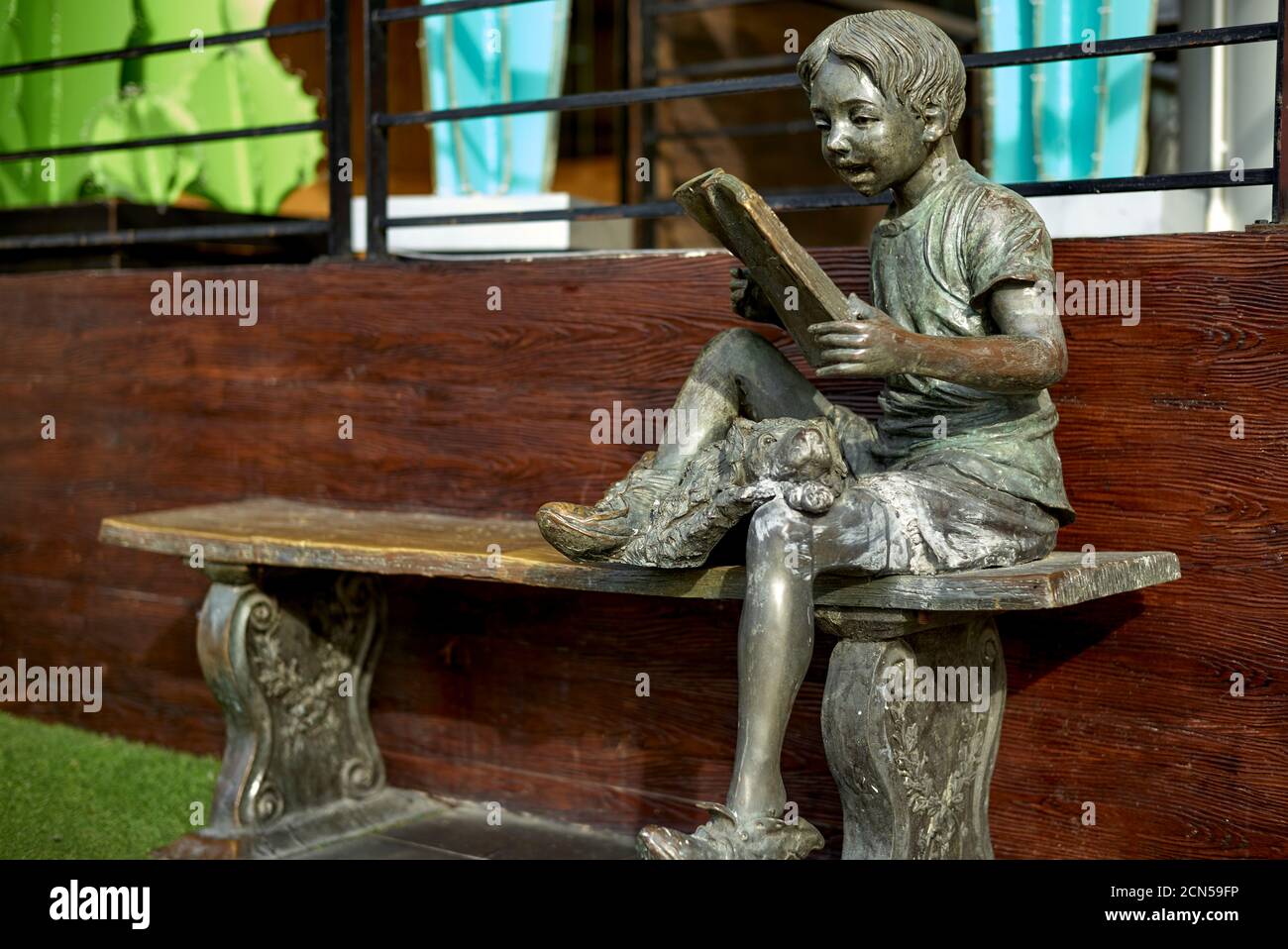 Statua di un ragazzo che si siede su una panchina e che legge un libro con un cane come suo compagno Foto Stock