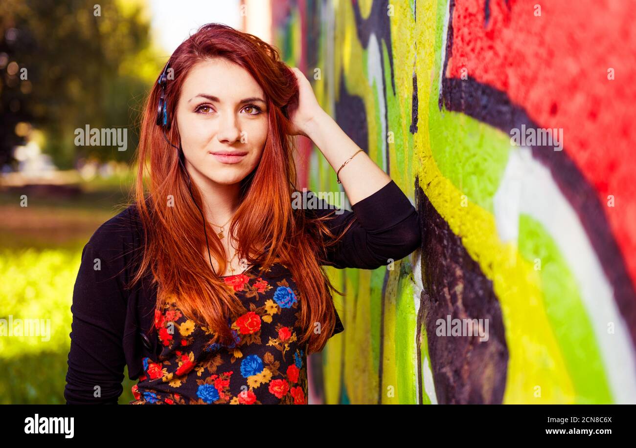 ritratto giovane donna rossa con cuffie sulla colorata parete dei graffiti Foto Stock